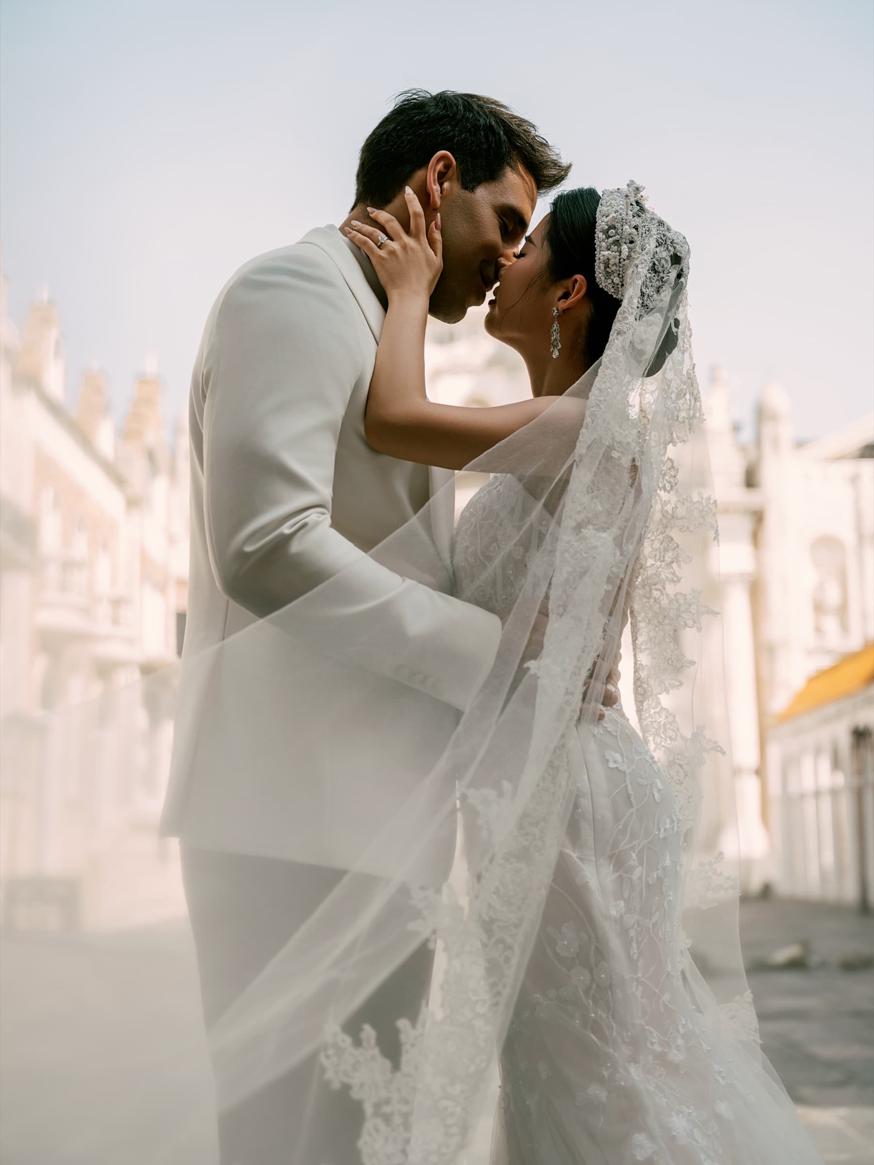 The couple kissing on a sunlit street, veil flowing in the wind