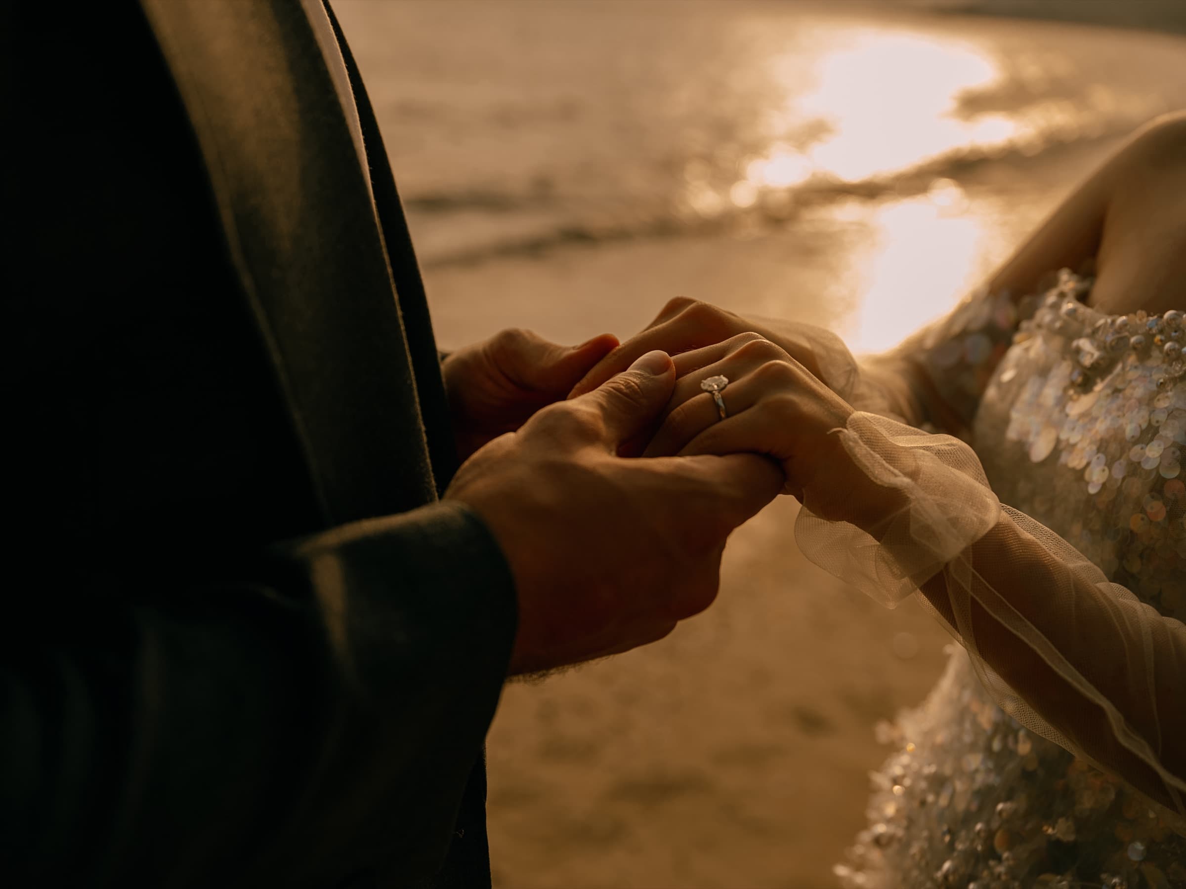 Close-up of the couple's hands and wedding ring at sunset by the sea
